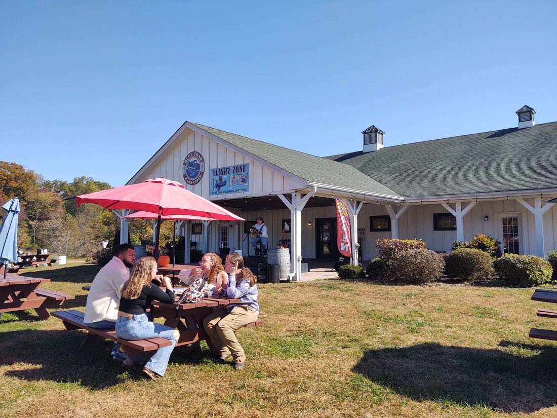 Picnic tables and umbrellas outside the taproom at Blue Toad Cidery, where the plates land on weekends